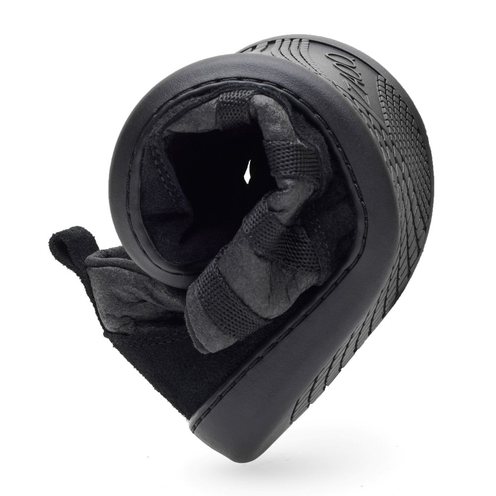 Nahaufnahme einer flexiblen, schwarzen Schuhsohle des ZAQQ SPARQ Low Pinatex Black, die spiralförmig gebogen ist, um ihre Textur und Flexibilität zu demonstrieren. Die Sohle besteht aus rutschhemmender Kautschuk für außergewöhnlichen Halt und weist ein gemustertes Design auf, während die Innenseite mit weichem, grauem Material ausgekleidet ist.