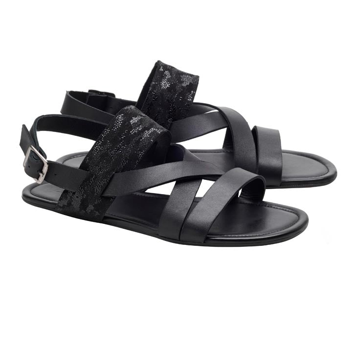 Ein Paar schwarze PERLAQ-Sandalen von ZAQQ mit überkreuzten Lederriemen mit silberner Schnalle und einem strukturierten schwarzen Stoffakzent am oberen Riemen, der das Nappaleder-Sandalendesign verkörpert. Diese Sandalen bieten mit ihrer flachen Sohle und dem offenen Zehenbereich höchsten Komfort.