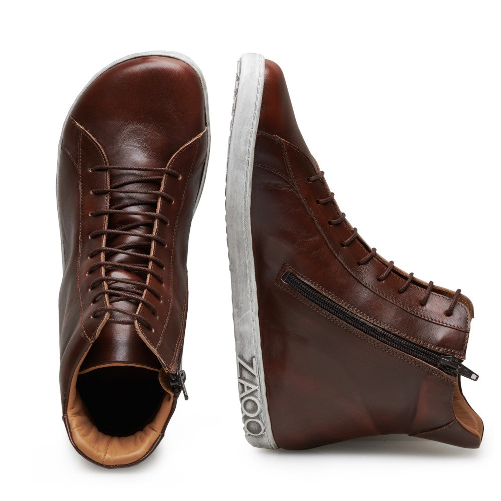 Ein Paar SNAQ Antique Brown High-Top-Sneaker aus Nappaleder mit weißer Sohle. Ein Schuh steht aufrecht und zeigt Schnürsenkel und Zehenpartie, während der andere auf der Seite liegt und einen seitlichen Reißverschluss und den Markennamen ZAQQ an der Ferse aufweist.