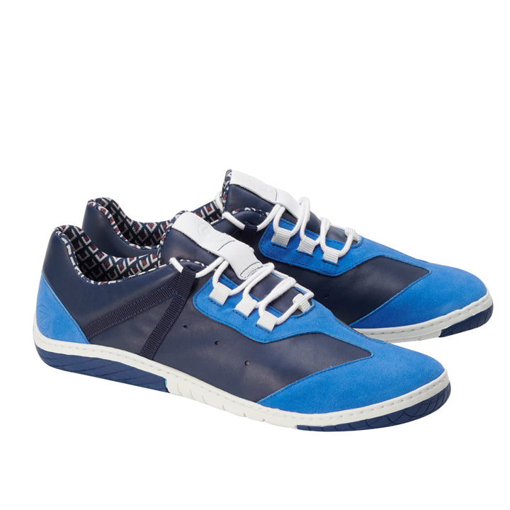 Die **QOAST Blue** Sneaker von **ZAQQ** sind ein Paar stylische Barfußschuhe in Blau und Marineblau mit weißer Sohle und Schnürsenkeln. Diese Schuhe haben ein Innenfutter mit einem farbenfrohen geometrischen Muster und bestechen durch ihr elegantes, modernes Design. Sie sind aus weichem Nappaleder gefertigt und sorgen für ultimativen Komfort.