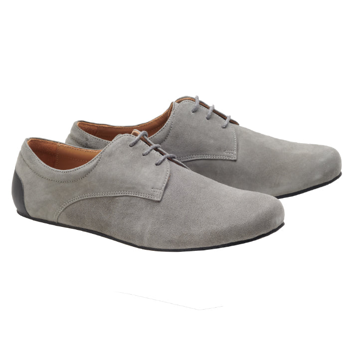 Der IQON Velours Grey von ZAQQ ist ein Paar hellgrauer Wildleder-Derbyschuh mit schlichtem Design, ideal als Business-Barfußschuh. Er verfügt über eine braune Innenausstattung und eine schwarze Sohle, zeigt einen klassischen Schnürstil und ist Teil der anspruchsvollen Business-Modell-Linie IQON.