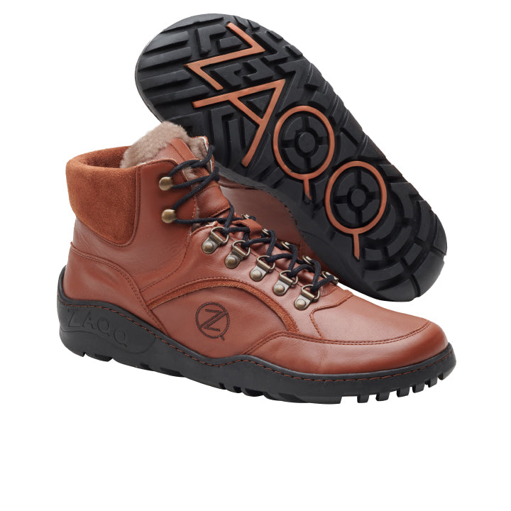 Ein Paar wasserdichte High-Top-Sneaker ZAQQ TREQ Cognac Winter aus braunem Leder mit schwarzen Gummisohlen. Diese stylischen Schuhe haben schwarze und braune Schnürsenkel, Metallösen und ein eingraviertes Logo an der Seite der Sohle. Das markante Profilmuster mit kreisförmigen Mustern bietet außergewöhnlichen Halt für Outdoor-Abenteuer.