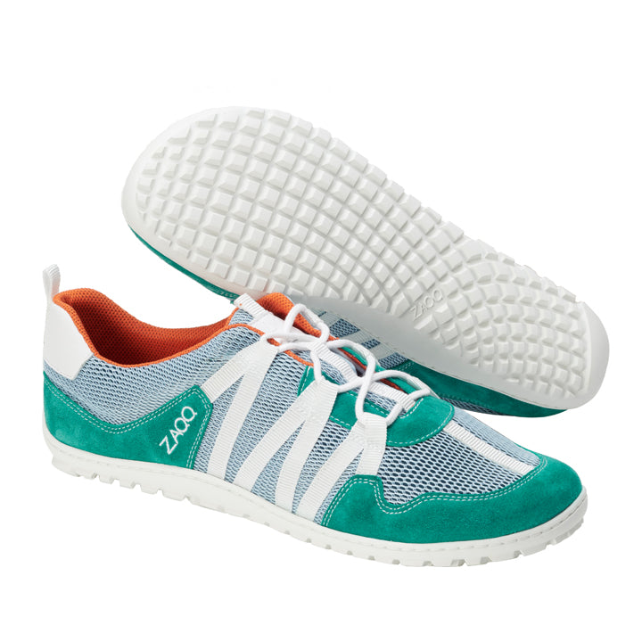 Die RIQ Turquoise Sportschuhe von ZAQQ präsentieren ein lebendiges türkis-weißes Design mit Mesh-Details und orangefarbenem Innenfutter. Als Barfußschuh sind diese Schuhe mit Veloursleder-Akzenten für zusätzlichen Stil versehen und bieten Atmungsaktivität gepaart mit einer flexiblen weißen Sohle mit strukturiertem Griff. Das ZAQQ-Branding ist deutlich an der Seite zu sehen.