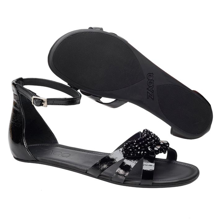 Die ZAQQ QISELLE Black Sandalen sind aus schwarzem Lackleder gefertigt und zeigen ein perlenbesetztes Blumenmuster auf dem vorderen Riemen. Diese eleganten Sandalen haben einen Knöchelriemen mit Schnalle und eine flache Sohle. Eine Sandale ist nach oben gerichtet, während die andere nach unten zeigt, wodurch jeder schicke Winkel hervorgehoben wird.