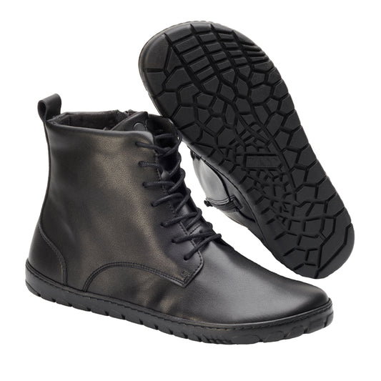 Ein Paar elegante ZAQQ QUINTIC Vegan Black-Stiefel mit Schnürsenkeln und einer strukturierten Gummi-Außensohle, ein Stiefel aufrecht und der andere geneigt, um das Design der Sohle hervorzuheben.