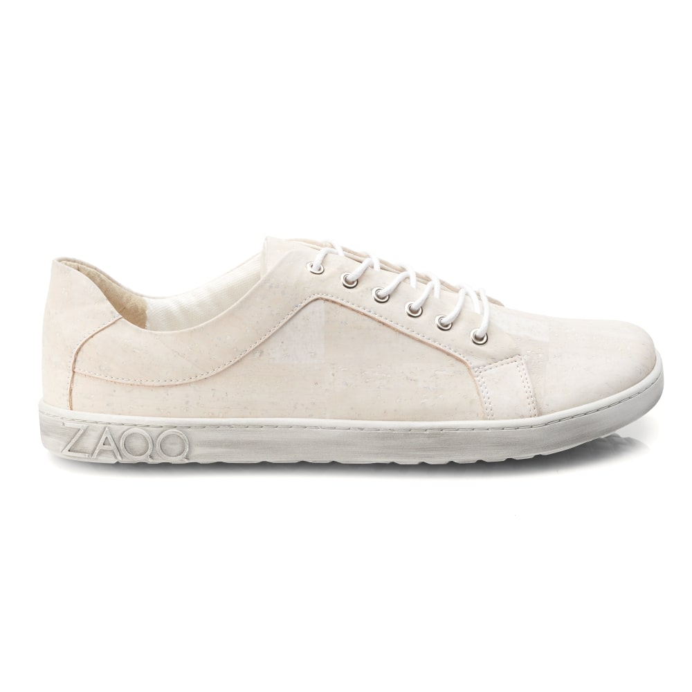 Seitenansicht des QORE Low Vegan White Sneakers von ZAQQ, der seine beige Farbe mit weißen Schnürsenkeln und einem geprägten Logo auf der Sohle zeigt. Der Schuh ist aus Kork-Obermaterial gefertigt und bietet ein minimalistisches Design mit strukturierter Oberfläche und einer stromlinienförmigen Silhouette.