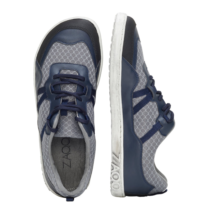 Wir präsentieren die ZAQQ SQATE Grey Sportschuhe – ein Paar graue und marineblaue Sneaker, ideal für jeden aktiven Tag. Diese Damen-Sneaker verfügen über ein atmungsaktives Netzmuster, weiße Sohlen und dunkelblaue Schnürsenkel. Ein Schuh steht aufrecht, der andere zeigt sein schlankes Seitenprofil und kombiniert so Stil mit Komfort.