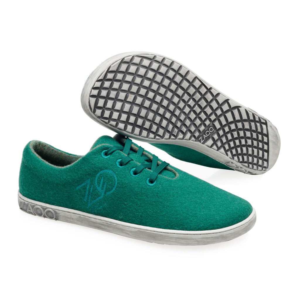 Ein Paar LIQE Green Casual Sneakers von ZAQQ mit weißer Sohle. Ein Schuh liegt flach, während der andere die Sohle mit Gittermuster zeigt. Das Logo ist sowohl an der Seite als auch an der Sohle zu sehen und unterstreicht den modernen Stil eines Barfußschuhs.