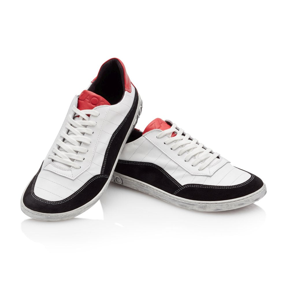 Wir präsentieren den eleganten QAMPION Black White von ZAQQ. Dieser stylische Barfuß-Sneaker zeichnet sich durch dynamische weiße, schwarze und rote Details aus und hat flexible Sohlen für mehr Komfort. Er verfügt über strahlend weiße Schnürsenkel, glatte schwarze Seiten und auffällige rote Akzente an Zunge und Ferse. Ein Schuh wird aufrecht präsentiert, während sein Partner anmutig dagegen lehnt.