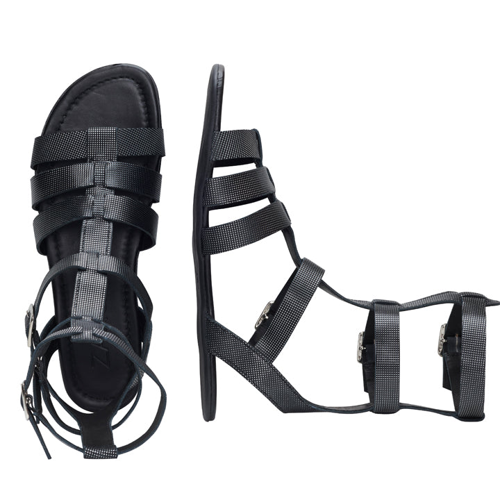 Schwarze Sandalen im Gladiator-Stil aus der QORA Black Silver-Kollektion von ZAQQ mit mehreren Riemen und Schnallen. Eine Sandale steht aufrecht, um eine Seitenansicht zu zeigen, während die andere flach liegt, um die Draufsicht zu zeigen. Beide Sandalen verfügen über einen Reißverschluss auf der Rückseite – ideal für einen extravaganten Modestil.