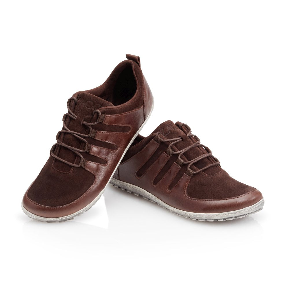 Die SHOQQ Dark Brown Sneaker von ZAQQ bestehen aus Leder mit Wildlederakzenten und einem markanten Schnürdesign, ergänzt durch Gummisohlen, die einen starken Kontrast zum weißen Hintergrund bilden. Diese Elemente verleihen dem Sneaker einen lässigen und dennoch stilvollen Look und machen ihn zu einem idealen Barfußschuh für jeden Anlass.