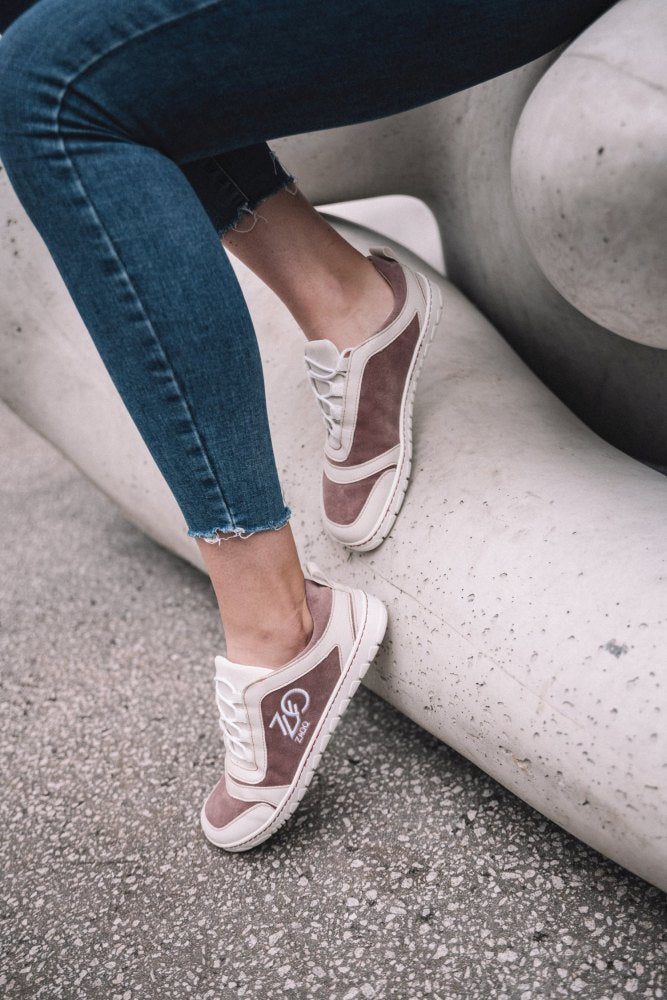 Eine Person in Jeans und stylischen SQILL Rose Sneakers von ZAQQ sitzt auf einer glatten, geschwungenen Betonkonstruktion. Das Design zeigt ein Monogramm der Buchstaben JP mit der Zahl 73 in Weiß auf rosa Hintergrund, gefertigt aus veganer Mikrofaser.