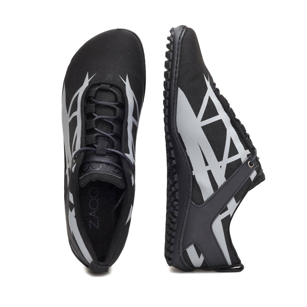 Der XIQOT Black von ZAQQ ist ein Paar schwarzer Sportschuhe mit kontrastierenden hellgrauen geometrischen Mustern und minimalistischem Design. Sie sind aus veganem Netzgewebe gefertigt und verfügen über eine flexible Gummisohle und elastische Schnürsenkel für bequemes Reinschlüpfen. Ein Schuh steht aufrecht, während der andere auf der Seite liegt, was ihre schlanke Bauweise unterstreicht.