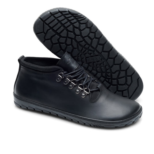 Ein Paar modische ZAQQ EXPEQ Mid Black Waterproof Lederschuhe mit Schnürsenkeln und auffälligen, strukturierten Gummisohlen. Ein Schuh steht aufrecht, während der andere auf die Seite geneigt ist und das detaillierte Sohlendesign zur Schau stellt.